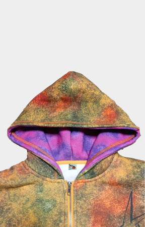 A close-up of a Dry Rot Acid Dust Zip Up Hoodie/sweatshirt with a multicolor tie-dye pattern in orange, yellow, green, and purple, featuring a purple-lined hood and a gold zipper.