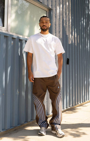 Discover the EPTM Flasher Pants in Brown/Blue, featuring bold pop-color tape and signature 3M reflective accents. Made from 100% polyester, these track pants include an elastic drawstring waistband, front welt pockets, a back pocket, and adjustable bottom toggles. A distinctive streetwear option for styling with graphic tees, hoodies, and sneakers.