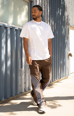 Discover the EPTM Flasher Pants in Brown/Blue, featuring bold pop-color tape and signature 3M reflective accents. Made from 100% polyester, these track pants include an elastic drawstring waistband, front welt pockets, a back pocket, and adjustable bottom toggles. A distinctive streetwear option for styling with graphic tees, hoodies, and sneakers.