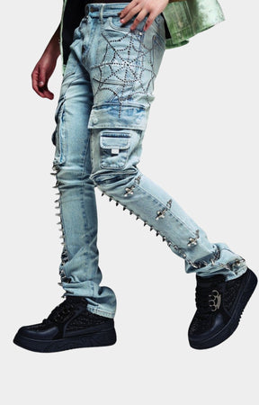 Guapi aqua blue distressed denim cargo pants with silver rhinestone spiderweb embroidery on the thigh, metal studs down the leg, and ripped details. 