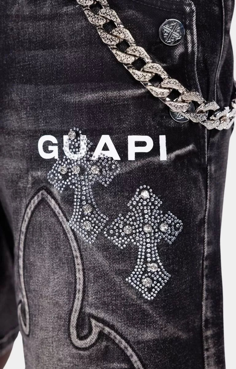Close-up detail of Guapi Obsidian Black Faded Cross denim shorts with metallic chain. 