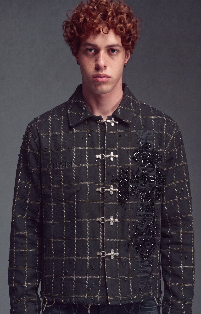 Obsidian Black Grid Shirt a black shirt featuring gold grid lines, silver toggle closures, and a large black beaded guapi signature cross branding on the right chest.