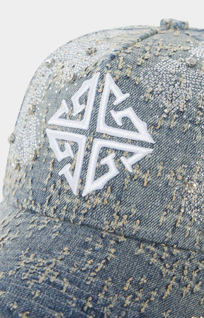 Close-up of 3D embroidered GUAPI cross logo on denim cap.