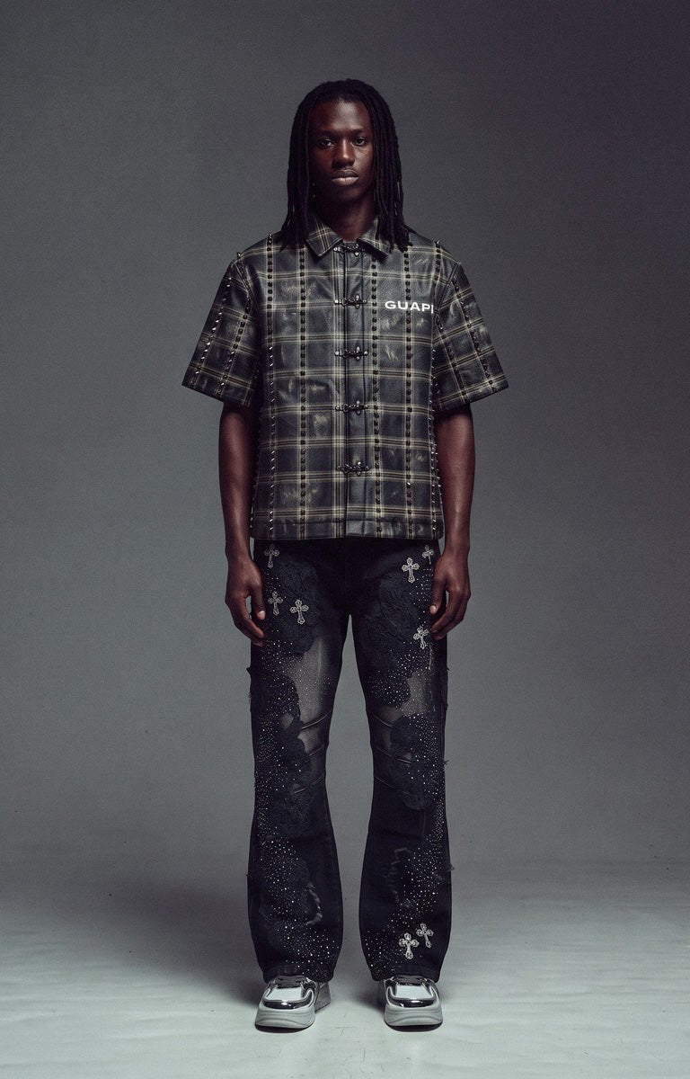 Guapi Obsidian Black No Hugs Shirt. short-sleeve plaid button-up shirt in black and gray, paired with dark distressed jeans featuring white cross motifs and white sneakers.