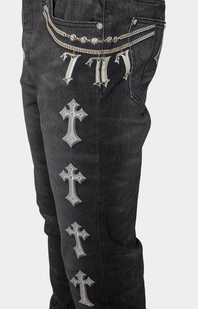 Side view showing rosary and metallic strap prints on Guapi black denim jeans with faux embellishments.