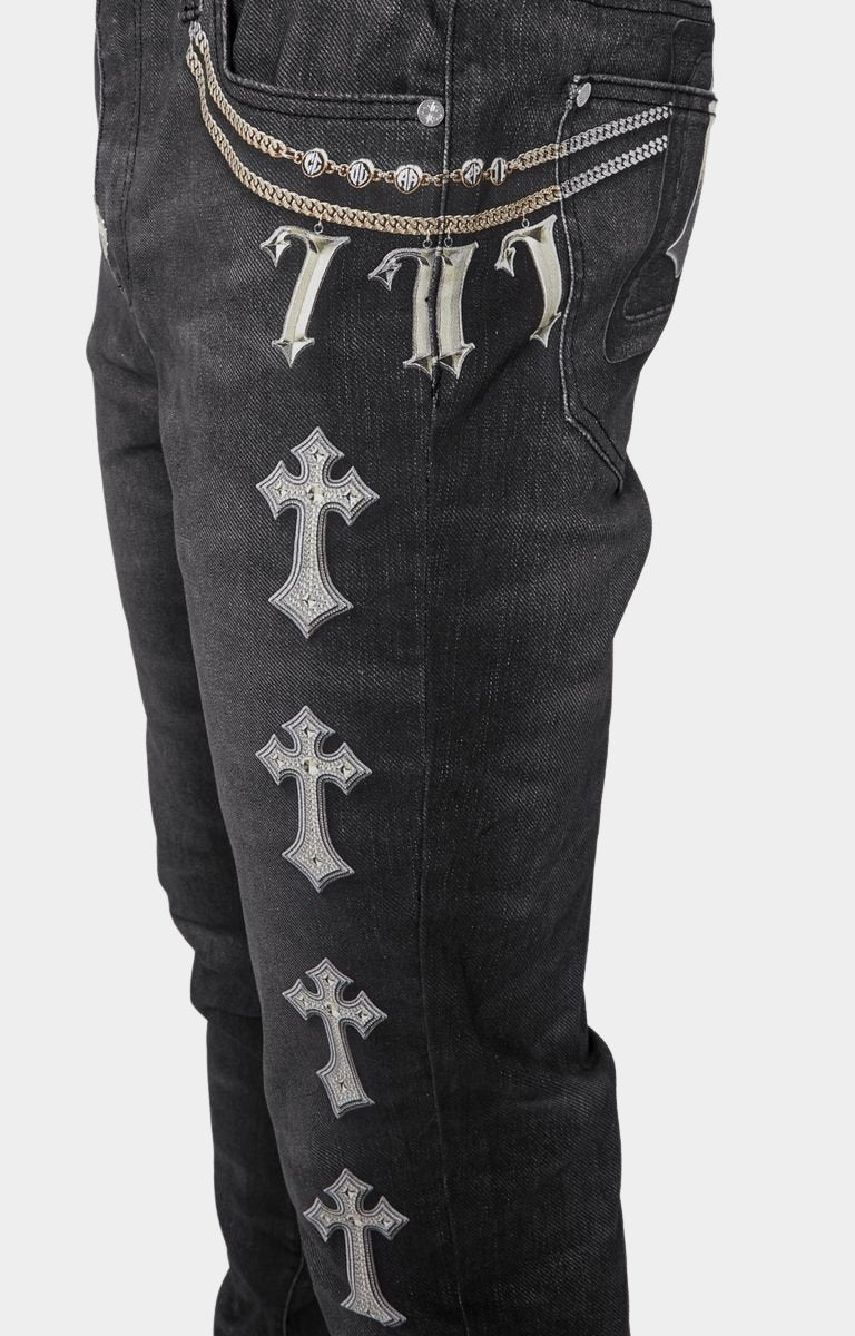 Side view showing rosary and metallic strap prints on Guapi black denim jeans with faux embellishments.