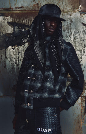 The GUAPI Obsidian Black Plaid Jacket pairs soft, fuzzy black plaid fabric with contrasting textured sleeves, scattered pearl embellishments, and a bold tonal embroidered back graphic. Metal front closures and ribbed cuffs and hem complete the relaxed silhouette. A distinctive designer streetwear jacket for styling with denim, cargos, and layered outfits.