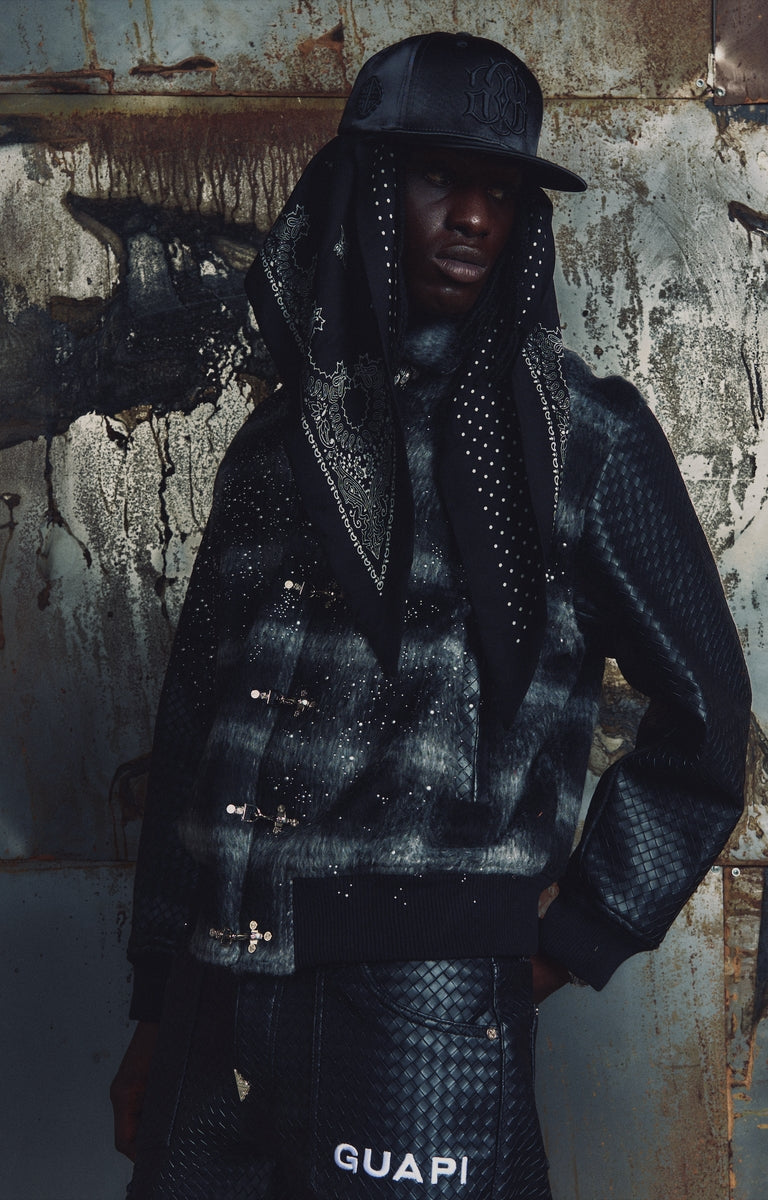 The GUAPI Obsidian Black Plaid Jacket pairs soft, fuzzy black plaid fabric with contrasting textured sleeves, scattered pearl embellishments, and a bold tonal embroidered back graphic. Metal front closures and ribbed cuffs and hem complete the relaxed silhouette. A distinctive designer streetwear jacket for styling with denim, cargos, and layered outfits.