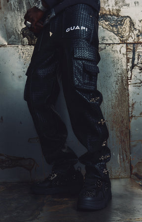 GUAPI Obsidian Woven Cargo Pant in Black features a distinctive woven texture, multiple utility cargo pockets, adjustable side buckle details, and signature GUAPI branding. Designed with a relaxed cargo silhouette, these statement pants pair with graphic tees, oversized hoodies, and contemporary streetwear outfits.