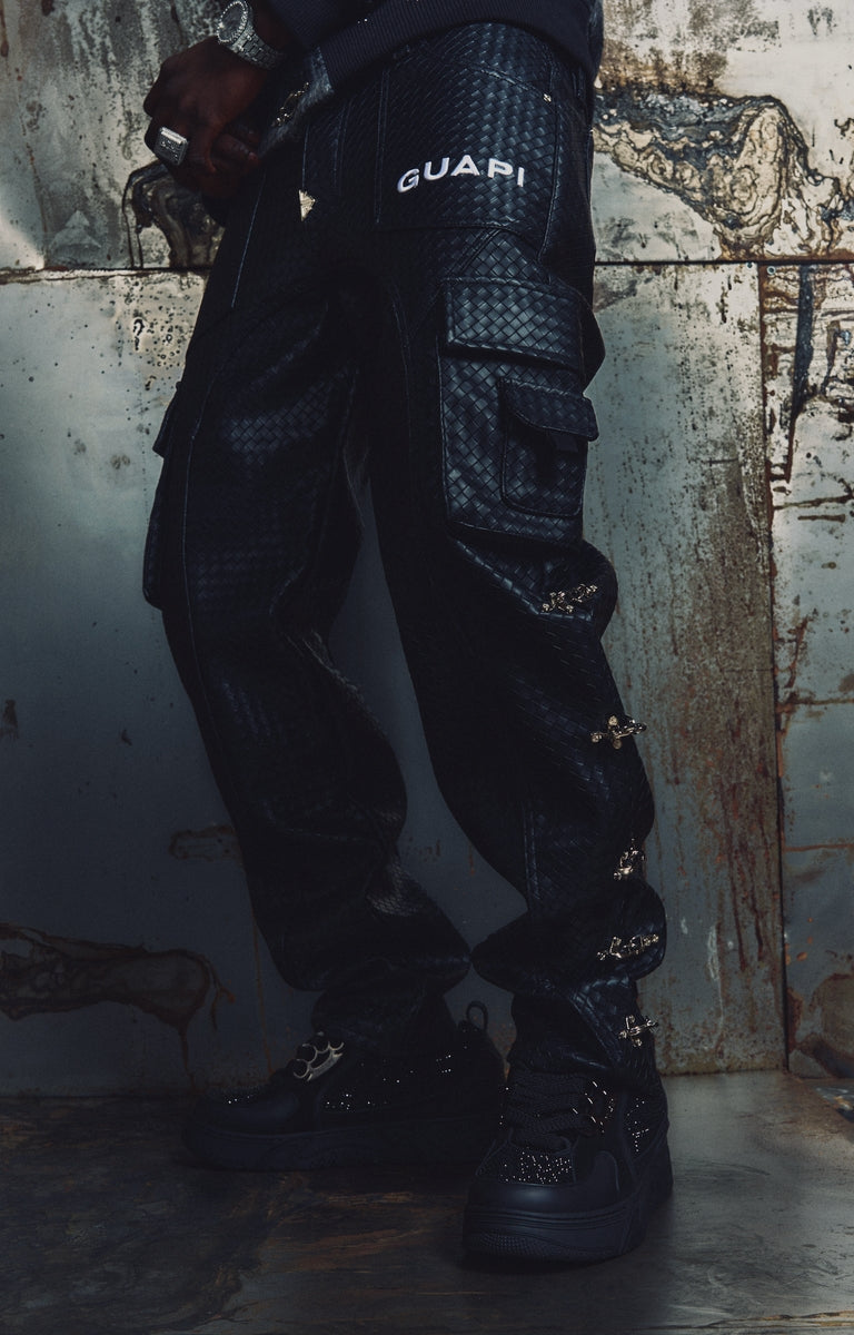 GUAPI Obsidian Woven Cargo Pant in Black features a distinctive woven texture, multiple utility cargo pockets, adjustable side buckle details, and signature GUAPI branding. Designed with a relaxed cargo silhouette, these statement pants pair with graphic tees, oversized hoodies, and contemporary streetwear outfits.