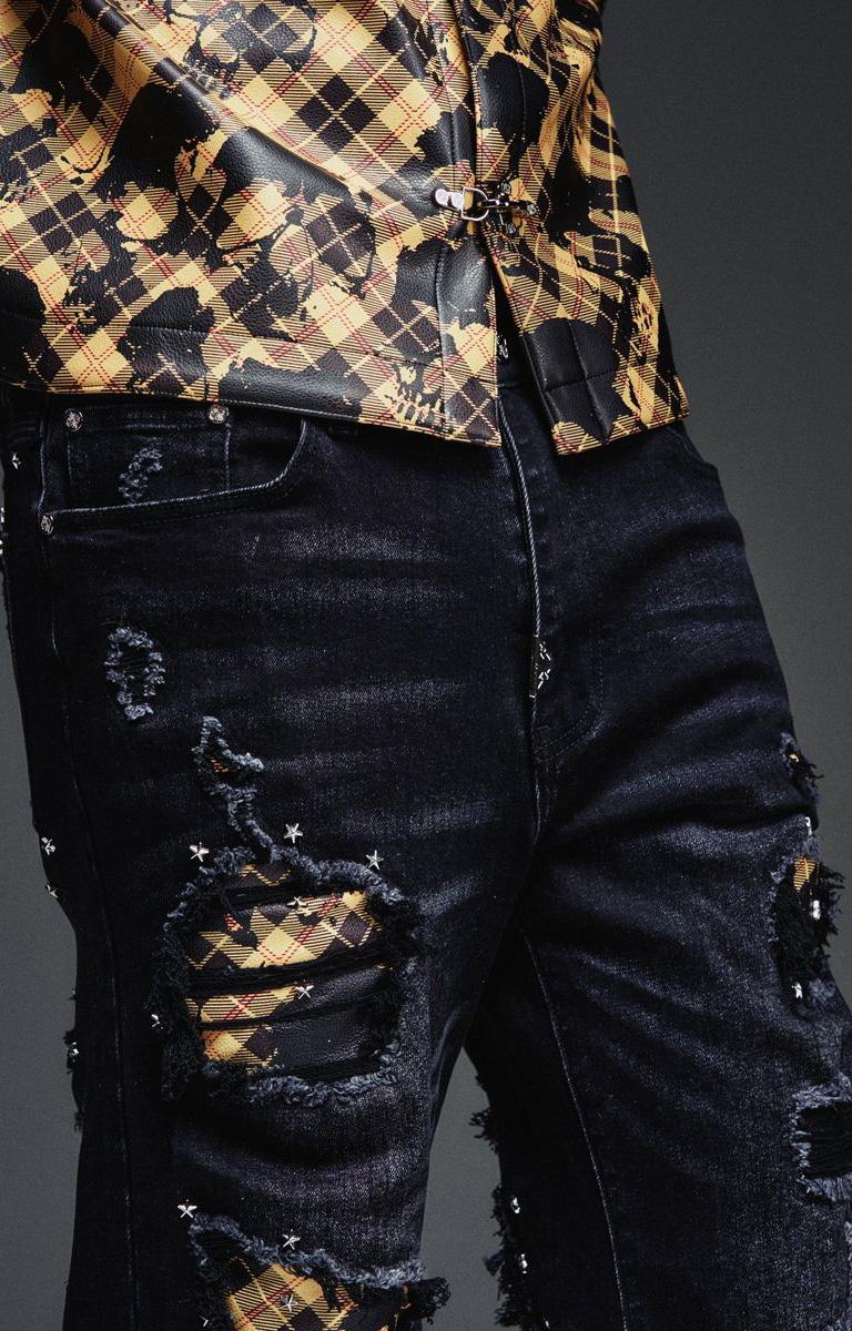 Close-up of GUAPI black denim showing ripped-effect details and plaid fabric inserts.