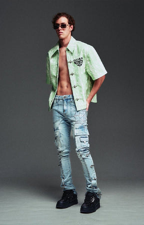 A male model wearing Guapi light green short-sleeve button-up shirt with a black Gucci logo on the chest, aqua blue light-wash distressed jeans, and black sneakers.