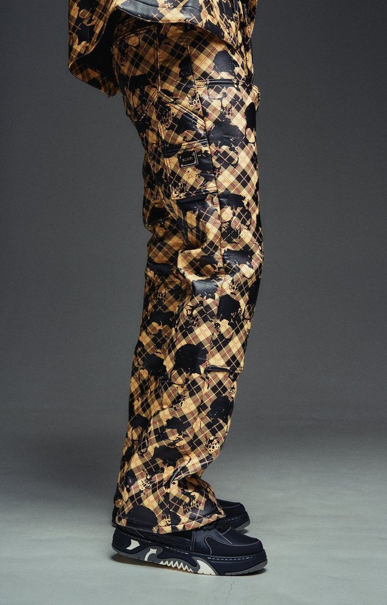 Guapi leather pants featuring bold skull plaid print patterned cargo-style with a tan, black, and brown plaid design, paired with dark sneakers.