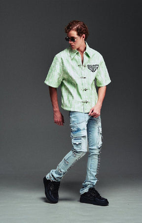 Guapi light green and white checkered short-sleeve button-up shirt with a black graphic logo on the chest, paired with distressed aqua blue jeans and black sneakers.