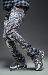 Guapi Hakai Spider stacked denim jeans with slim streetwear fit, distressed, graffiti-style black and white patterned jogger pants with gray and white high-top sneakers.