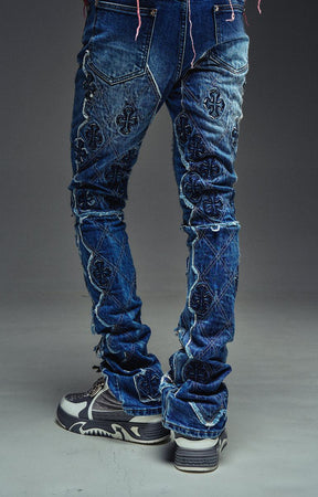Guapi Vintage Blue Relic Denim featuring a vintage wash, distressed patchwork, cross-inspired appliqué, slim thigh fit, subtle flare leg, and metallic detailing.