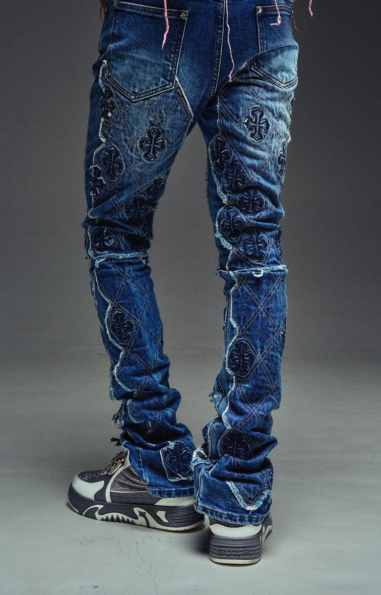 Guapi Vintage Blue Relic Denim featuring a vintage wash, distressed patchwork, cross-inspired appliqué, slim thigh fit, subtle flare leg, and metallic detailing.