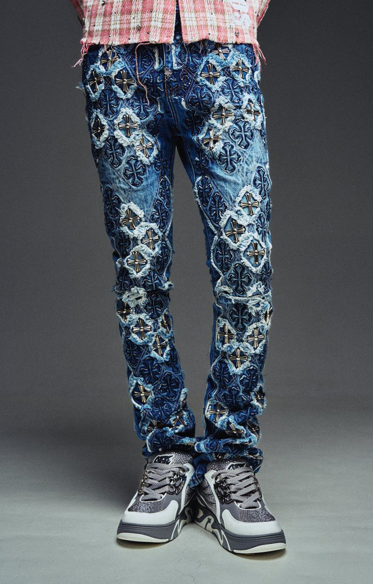 Guapi Vintage Blue Relic Denim featuring a vintage wash, distressed patchwork, cross-inspired appliqué, slim thigh fit, subtle flare leg, and metallic detailing.