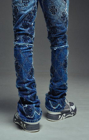 Guapi Vintage Blue Relic Denim featuring a vintage wash, distressed patchwork, cross-inspired appliqué, slim thigh fit, subtle flare leg, and metallic detailing.