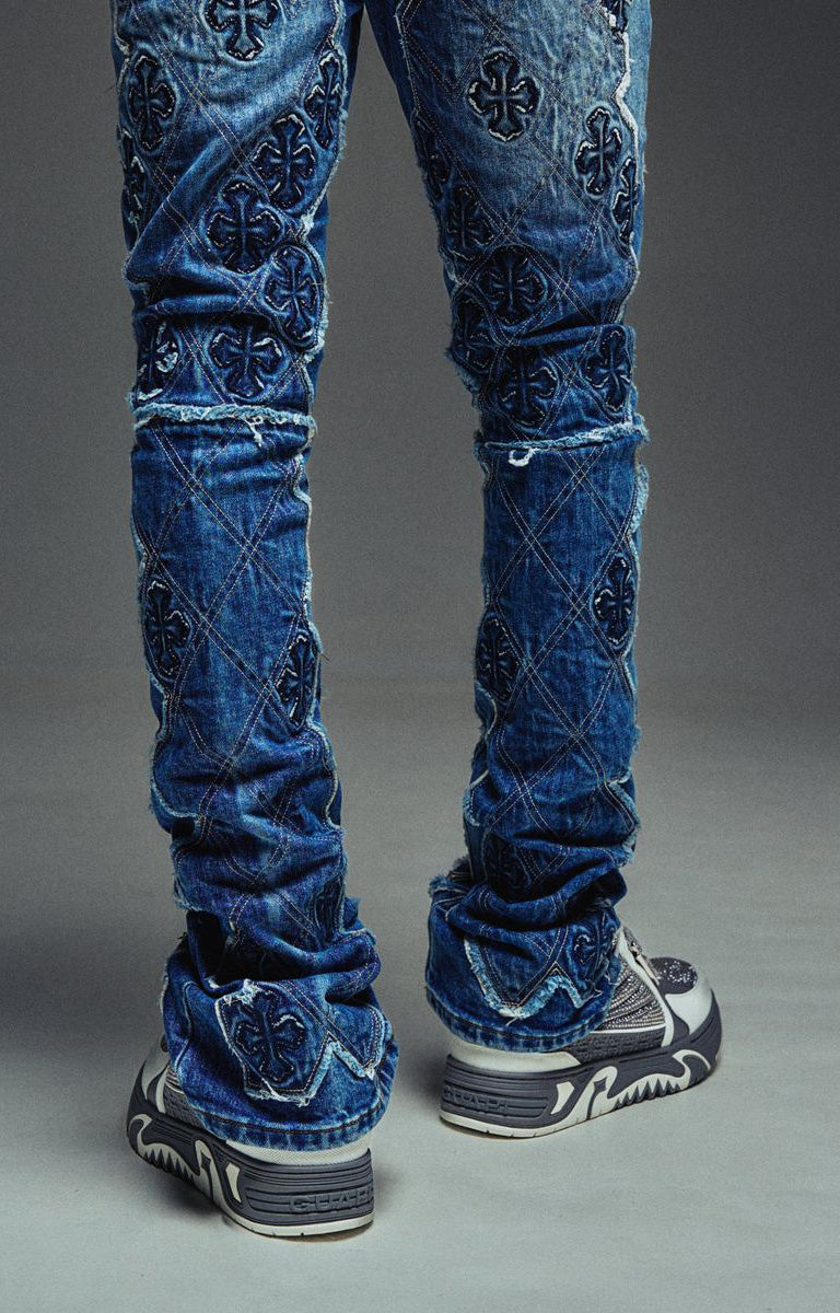 Guapi Vintage Blue Relic Denim featuring a vintage wash, distressed patchwork, cross-inspired appliqué, slim thigh fit, subtle flare leg, and metallic detailing.