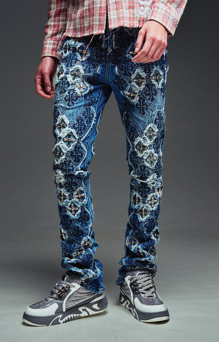 Guapi Vintage Blue Relic Denim featuring a vintage wash, distressed patchwork, cross-inspired appliqué, slim thigh fit, subtle flare leg, and metallic detailing.