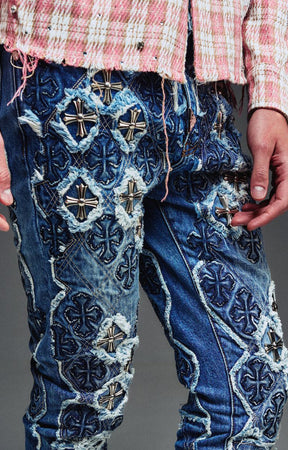 Guapi Vintage Blue Relic Denim featuring a vintage wash, distressed patchwork, cross-inspired appliqué, slim thigh fit, subtle flare leg, and metallic detailing.