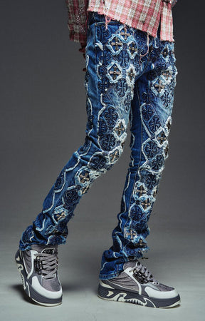 Guapi Vintage Blue Relic Denim featuring a vintage wash, distressed patchwork, cross-inspired appliqué, slim thigh fit, subtle flare leg, and metallic detailing.