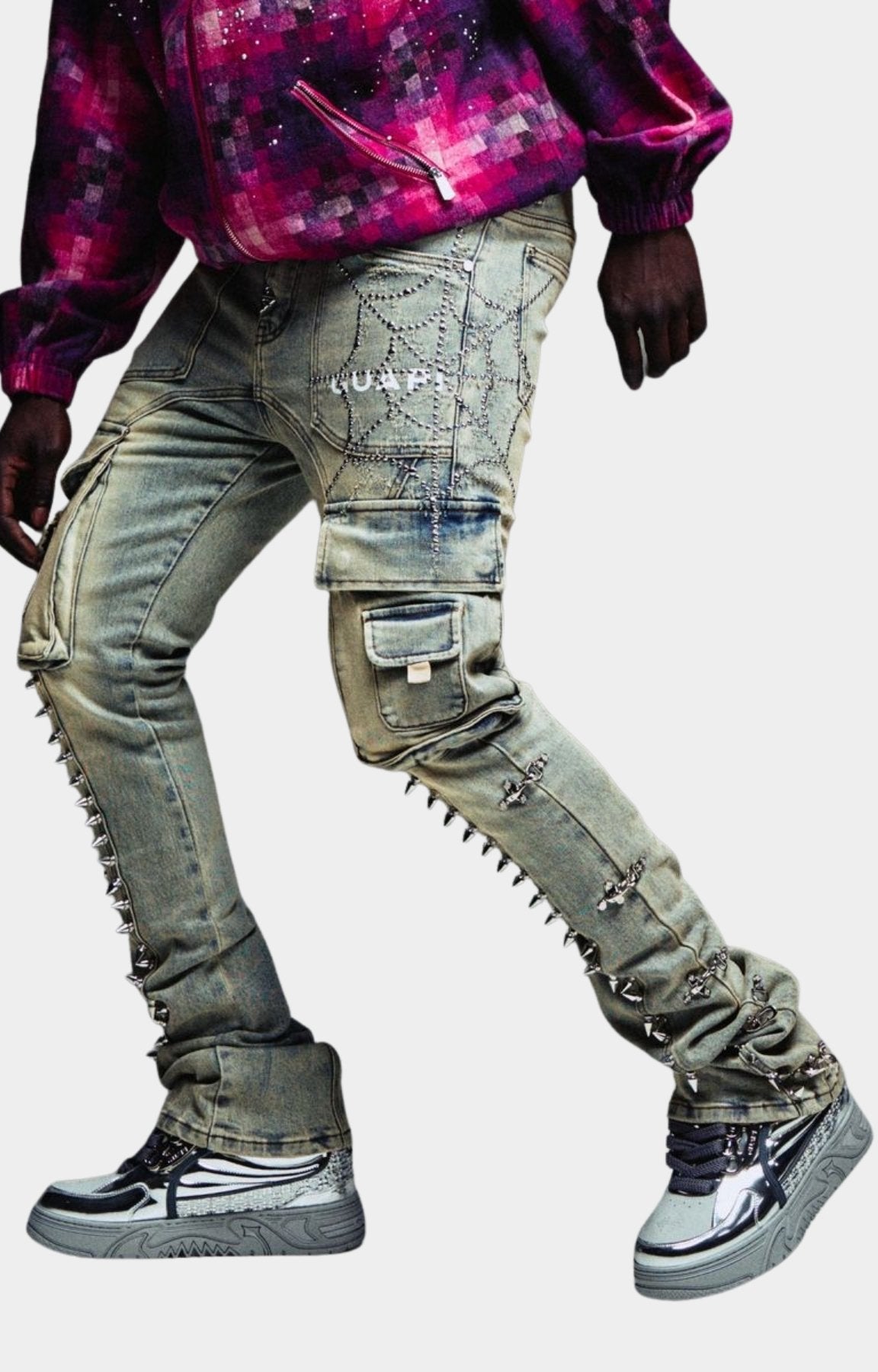 Guapi Vintage Spikes Cargo Denim in faded grey wash heavily distressed and embellished gray cargo-style jeans with metal studs, chain details, and ripped sections, paired with a purple patterned top and silver sneakers. 