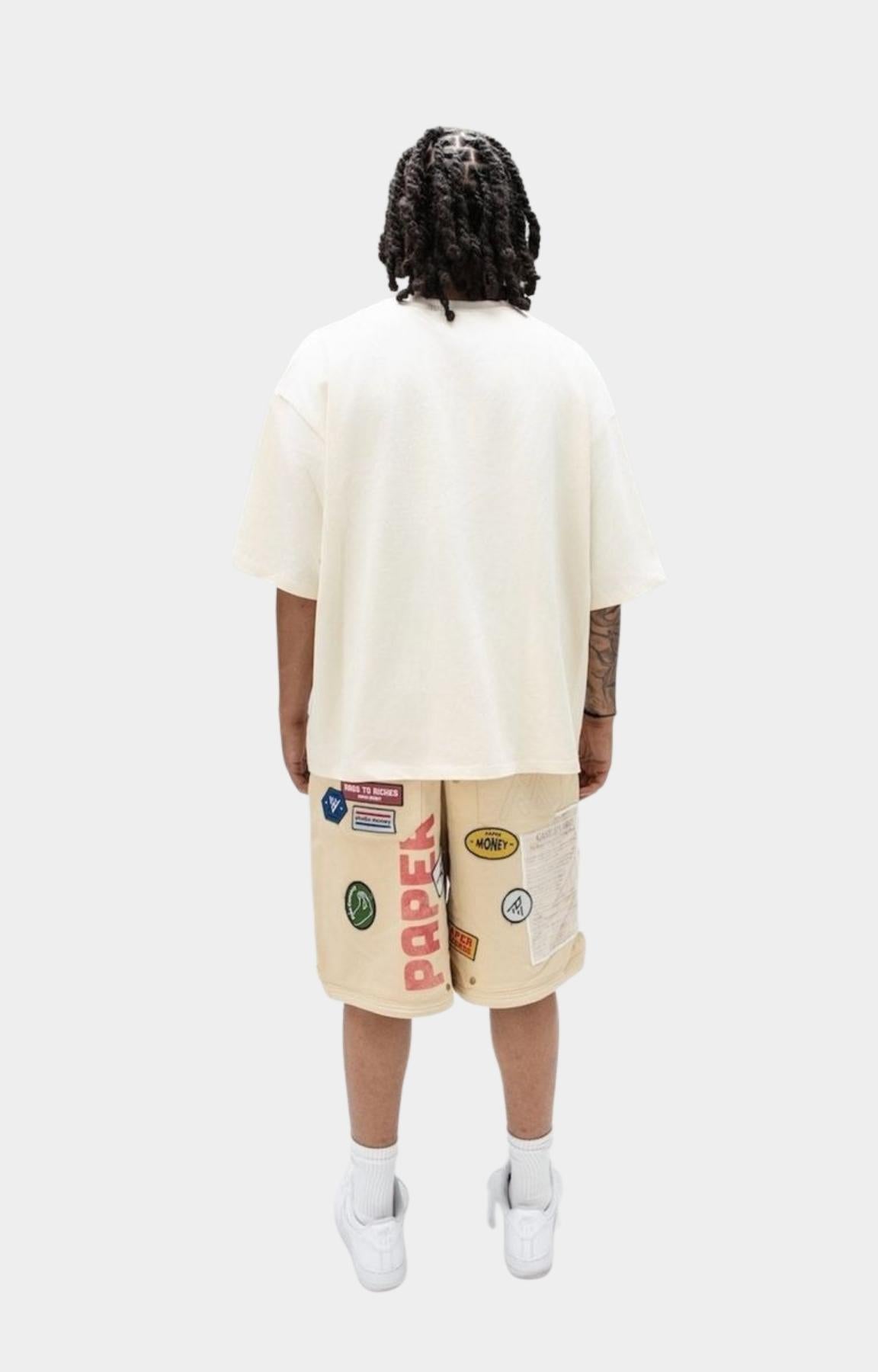 Oversized cream Paper Money graphic t shirt with beige shorts decorated with colorful graphic patches.