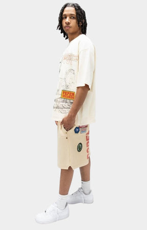 Angled view of Paper Money Paper States oversized graphic cream-colored graphic t-shirt and matching graphic shorts, paired with white socks and white sneakers.