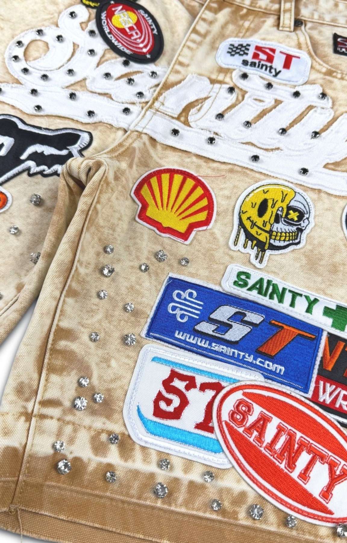 Khaki wash denim shorts featuring colorful embroidered racing-inspired patches.