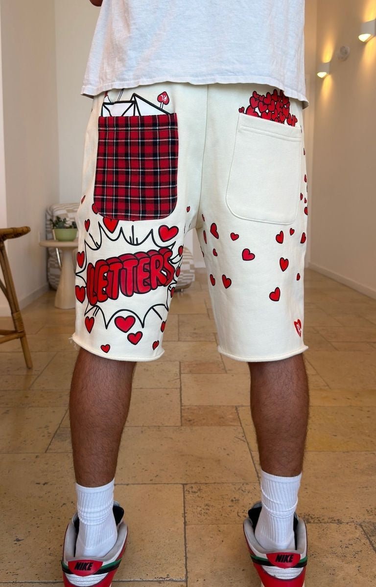 Red Letters off white cream-colored graphic 500 GSM sweat shorts with red hearts, a red plaid pocket, and 'LETTERS' text. 