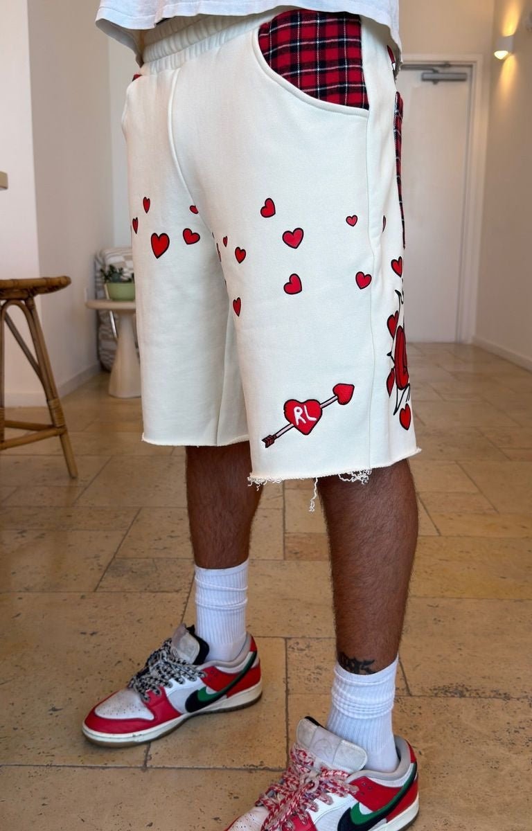 Red Letters off-white shorts with red heart prints, a red plaid pocket, and a red heart-and-arrow graphic near the hem, paired with white socks and red, white, and green sneakers.