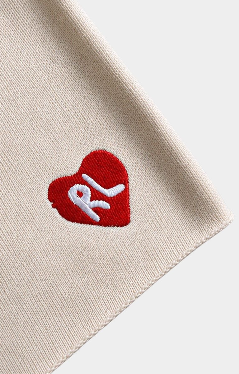 Close-up of a red letters cream-colored knit shorts fabric, featuring a red heart patch with a white embroidered 'RL' logo.