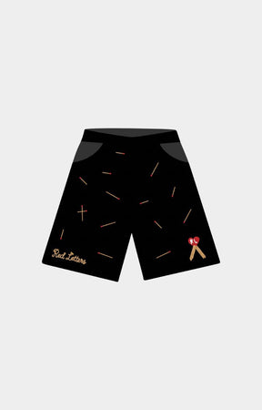 Red Letters Start the Fire 500 GSM Heavyweight French Terry Black athletic shorts with a scattered gold matchsticks pattern, featuring a gold 'Red Letters' script logo on the left leg and a small red and gold ribbon graphic on the right leg. 