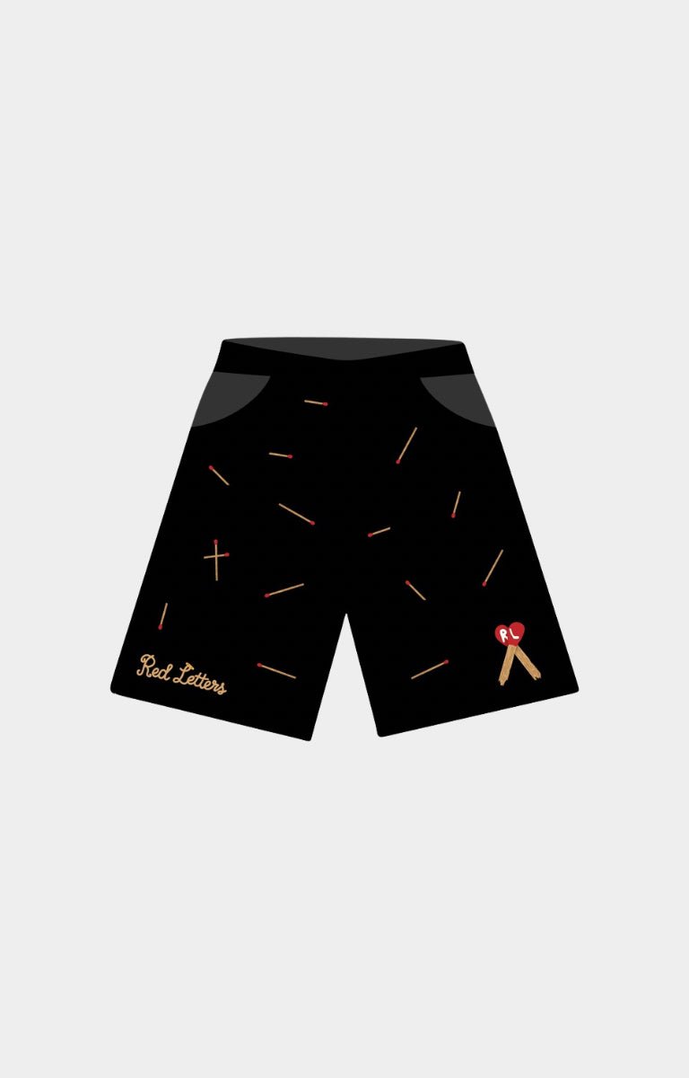 Red Letters Start the Fire 500 GSM Heavyweight French Terry Black athletic shorts with a scattered gold matchsticks pattern, featuring a gold 'Red Letters' script logo on the left leg and a small red and gold ribbon graphic on the right leg. 