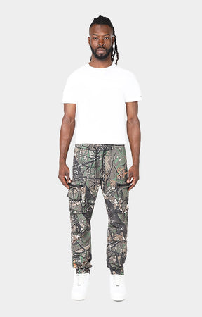 Smoke Rise camouflage cargo jogger pants with white sneakers. Utility leg detailing on Smoke Rise Tree Camo cargo pants. 