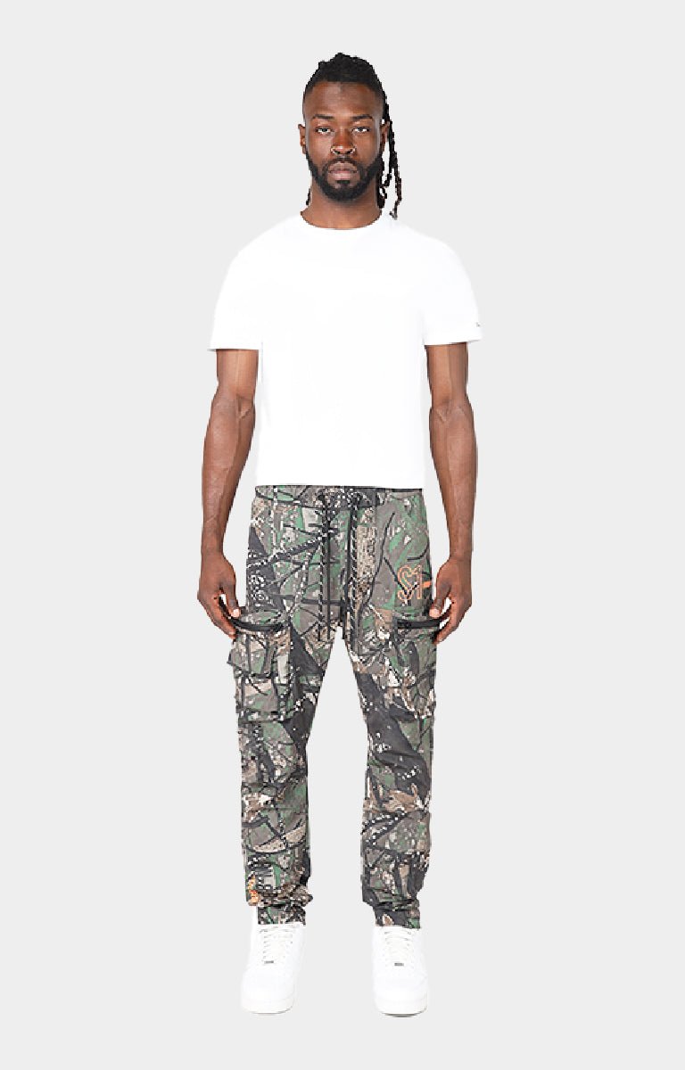 Smoke Rise camouflage cargo jogger pants with white sneakers. Utility leg detailing on Smoke Rise Tree Camo cargo pants. 