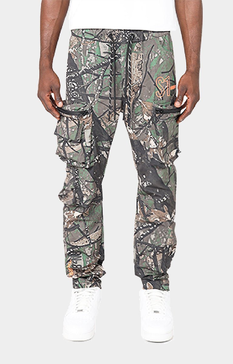 Smoke Rise camouflage cargo jogger pants front view with multiple flap pockets, a drawstring waist, and elastic cuffs, paired with white sneakers.