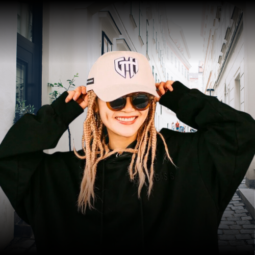Woman in oversized black hoodie and beige streetwear cap smiling outdoors